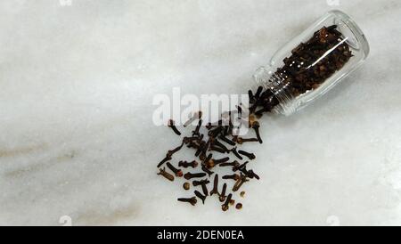 Vista dall'alto di chiodi di garofano asciutti che fuoriescono da una bottiglia di vetro su una superficie di marmo. Foto Stock