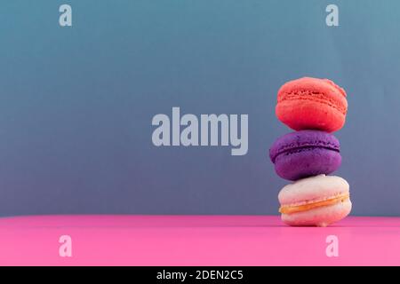 Primo piano di macaron bianchi, viola e rosa accatastati su sfondo rosa e blu Foto Stock