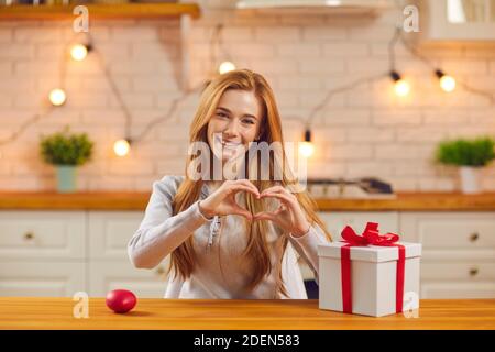 La donna sorridente mostra il cuore davanti alla telecamera, esprimendo l'amore al suo amante durante una videochiamata. Foto Stock