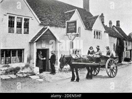 Vecchia fotografia di Graystone Bird del White Hart Inn, Castle Combe, Wiltshire. Una tazza di sidro è servita fuori dal pub come un carro e un cavallo in attesa. Foto Stock