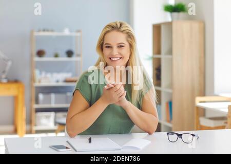 Smiling woman online conduce un webinar aziendale attraverso una videoconferenza seduta in ufficio. Foto Stock