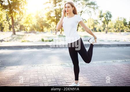 Giovane ragazza flessibile, che parla al telefono e stirata, prima di fare jogging, può essere utilizzato per la pubblicità, Foto Stock