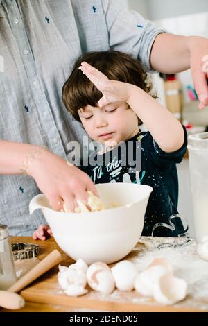 Ragazzino che aiuta la madre con la cottura in cucina in piedi al bancone accanto alla sua impastatura l'impasto per la torta Foto Stock