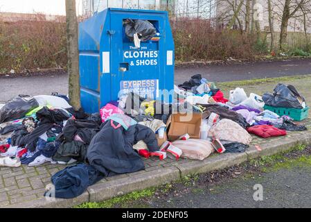 Indumenti e scarpe traboccanti riciclare unità di raccolta beneficenza con abiti sparsi intorno ad esso Foto Stock