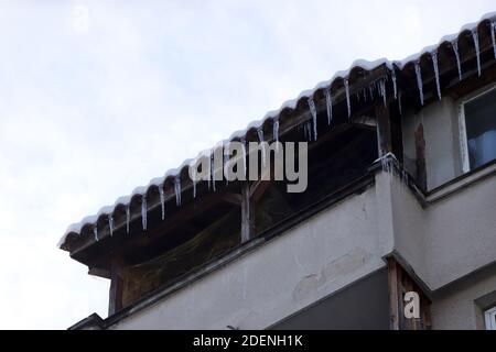 Le ciclicole pericolose pendono dal bordo di un tetto sopra una strada. Pericolo pendenti di ghiaccio Foto Stock