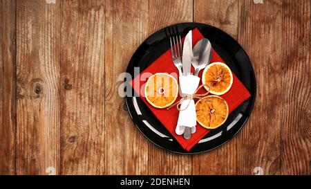 Decorazione della cena di Natale con arance secche e un tovagliolo rosso su un piatto nero su sfondo di legno. Spazio per il testo Foto Stock