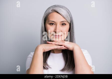 Foto ritratto di anziana bella donna con capelli grigi mantenimento mani vicino al mento sorridenti isolate su sfondo grigio Foto Stock