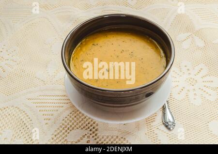 Su uno sfondo lacey c'è una ciotola a strisce marroni di zuppa di zucca densa e meatless. Foto Stock