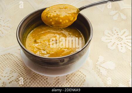 Un cucchiaio sta sollevando la zuppa di zucca liscia e spessa da una ciotola che si trova in un piccolo piatto bianco su una tovaglia di pizzo. Foto Stock