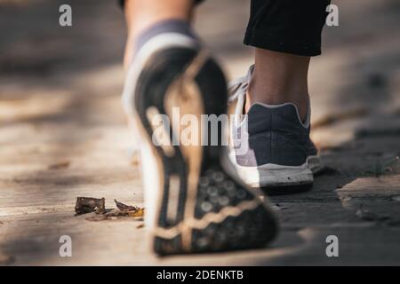 i piedi di una ragazza bianca passeggiando lungo un percorso di legno in sneakers e pantaloni neri con le caviglie in aria, facendo un passo con la suola della scarpa fuori Foto Stock