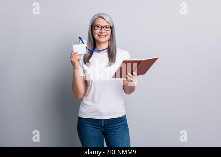 Foto di affascinante vecchia donna vestito casual abito occhiali mostrando scheda id che tiene il pianificatore isolato sfondo grigio Foto Stock