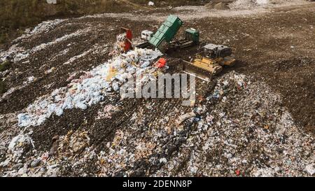 Vista del drone superiore del dump con diversi tipi di immondizia. I carrelli scaricano i rifiuti in discarica. Trattore giallo. Smistamento dei rifiuti. Foto Stock