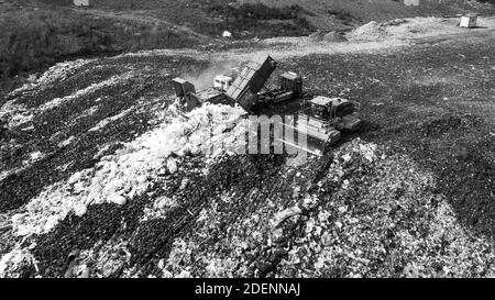 Vista del drone superiore del dump con diversi tipi di immondizia. I carrelli scaricano i rifiuti. Discarica della grande città. Bianco e nero. Foto Stock