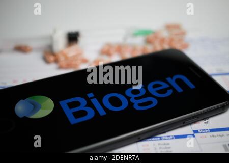 Viersen, Germania - 9 aprile. 2020: Primo piano dello schermo del telefono cellulare con la scritta del logo della società Biogen, pillole sfocate e sfondo del foglio di laboratorio Foto Stock