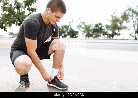 Atleta legando le sue scarpe squattando, primo piano, allenamento mattutino con un giovane Foto Stock