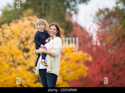 Una giovane madre e suo figlio giocano nel parcheggia contro splendidi colori autunnali che illustrano la felicità e la gioia di famiglia Foto Stock