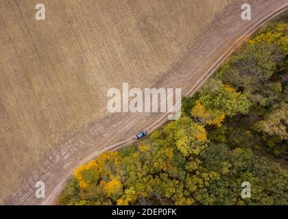 Vista aerea da un drone sopra la strada sterrata attraverso il campo agricolo e l'area forestale. Foto Stock