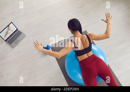 Donna che guarda la lezione di allenamento online e fa l'esercizio di estensione indietro montare la sfera Foto Stock