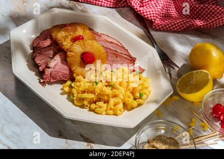 Cena al prosciutto di agrumi smaltato al miele arrosto con anelli di ananas a fette e le ciliegie di maraschino servite con un lato di pisello verde maccheroni e formaggio Foto Stock