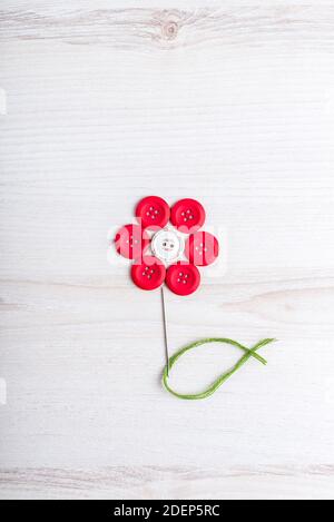 Tema cucito disegno creativo piatto: Fiore fatto di ago, filo e bottoni su superficie di legno Foto Stock