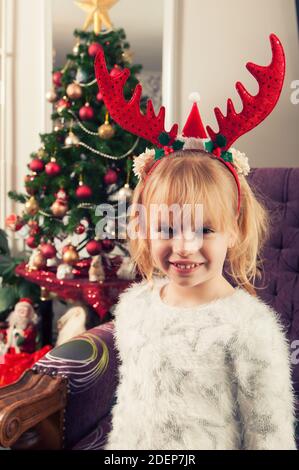 Bella bambina con corna, in piedi accanto all'albero di battesimo e sorridente Foto Stock