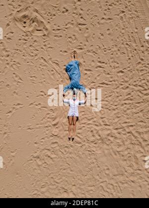 Divertente: Due dottori femminili in attrezzatura medica fanno angeli di sabbia sdraiati sulla spiaggia Foto Stock