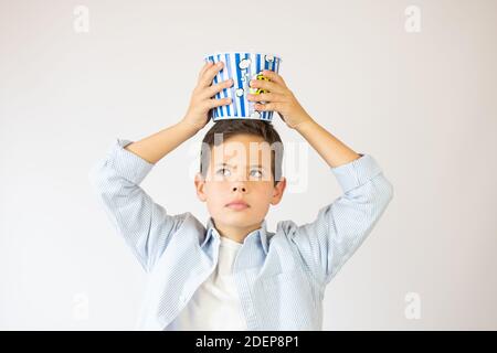 fast food, concetto di infanzia e di gente - ragazzo sorridente felice che mangia popcorn da bucket di carta a strisce su sfondo bianco Foto Stock