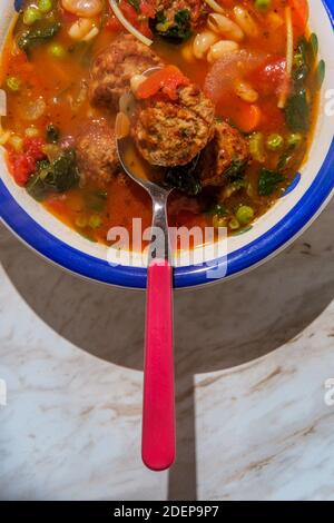 Zuppa di polpette di pomodoro con fagioli cannellini verdino di spinaci piselli e scorza di parmigiano Foto Stock