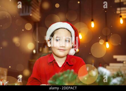 Bel ragazzo carino in berretto Babbo Natale su oro offuscato sfondo Foto Stock