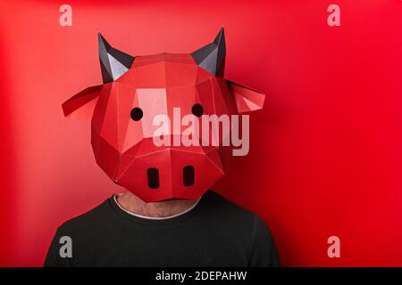 Giovane uomo in rosso maschera 3d di mucca toro sulla testa su uno sfondo isolato. Primo piano persona ritratto. Vuoto per banner, template, posto per pubblicità Foto Stock