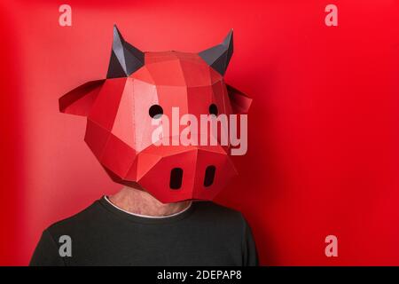 Giovane uomo in rosso maschera 3d di mucca toro sulla testa su uno sfondo isolato. Primo piano persona ritratto. Vuoto per banner, template, posto per pubblicità Foto Stock