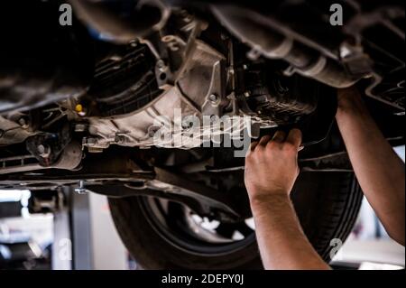 Primo piano delle mani dell'uomo che riparano un'auto sollevata Foto Stock