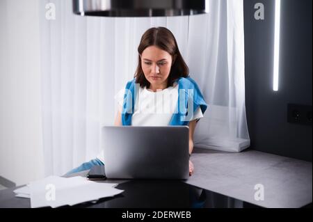 Giovane donna focalizzata che lavora sulle piccole imprese si avvia con un notebook. È seduta al suo tavolo da cucina a casa Foto Stock