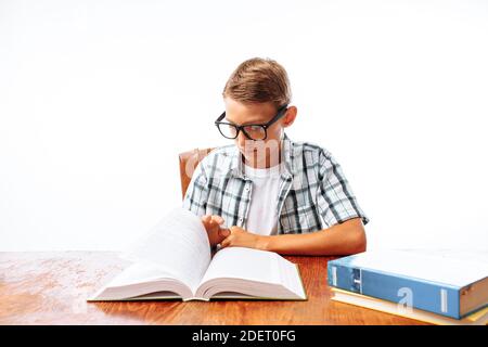 Giovane bel ragazzo che legge libro seduto al tavolo, scolaro o studente facendo compiti, in Studio su sfondo bianco Foto Stock