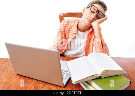 Teen guy si addormentò seduto con i libri su un computer portatile, studente dormendo alla scrivania in Studio Foto Stock