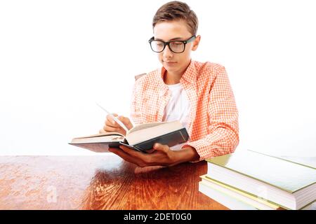 Giovane bel ragazzo che legge libro seduto al tavolo, scolaro o studente facendo compiti, in Studio su sfondo bianco Foto Stock