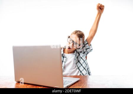 Un giovane seduto a un tavolo con un laptop, felice vittoria alzando la mano, seduto nello Studio Foto Stock