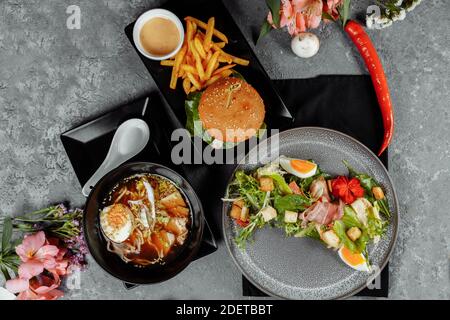 pranzo di lavoro di tre portate. Pranzo con hamburger di spaghetti asiatici ramen e insalata caesar. Foto Stock