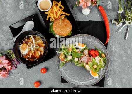 pranzo di lavoro di tre portate. Pranzo con hamburger di spaghetti asiatici ramen e insalata caesar. Foto Stock