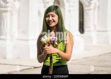 Giovane donna vestita di fiori verdi che tengono davanti alle pagode a Kuthodaw pagoda, Mandalay, Myanmar Foto Stock