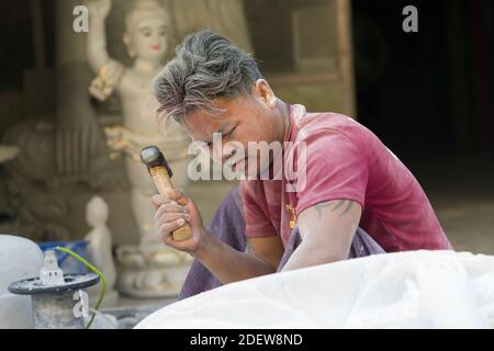 Intagliatore di marmo con martello mentre intagliando la statua del Buddha, Mandalay, Myanmar Foto Stock