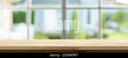 Tavolo in legno all'interno della casa con verde sfocato giardino esterno finestra sullo sfondo, banner panoramico - può essere utilizzato per la visualizzazione o montaggio del vostro prodotto Foto Stock