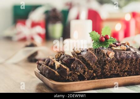 Deliziosa torta di frutta di Natale a base di nocciole essiccate su piastra di legno con scatole regalo colorate sfocate e oggetti decorativi in background Foto Stock