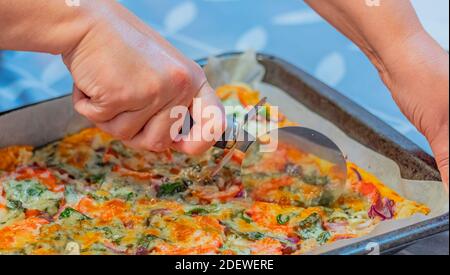 Donna che taglia la pizza fatta in casa con il rullo. Messa a fuoco selettiva, primo piano, concept photo food. Foto Stock