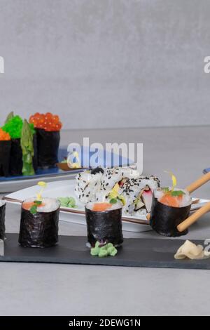 Primo piano di un assortimento di maki e uramaki su vassoi con bastoncini che raccolgono un pezzo maki. Concetto di sushi e cibo sano. Foto Stock