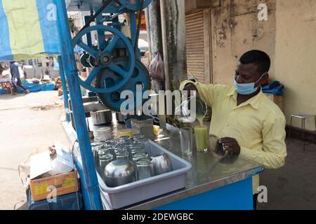 Goa India 11 novembre 2020 UN venditore di strada che versa canna da zucchero Spremere in bicchiere al Mapusa Market Goa Foto Stock