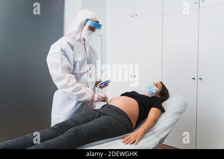 Un ginecologo esamina una donna incinta durante una pandemia di Covid 19. Auscultazione del cuore del doppler fetale. Foto Stock