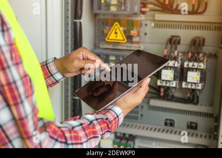 Primo piano del tecnico o dell'elettricista che lavora controllare l'impianto elettrico con il tablet in fabbrica. Foto Stock