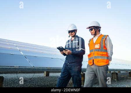 Ingegneri con investitore a piedi per controllare il funzionamento dei sistemi di fattoria solare (pannello solare), energia alternativa per conservare il mondo è energia, Photov Foto Stock