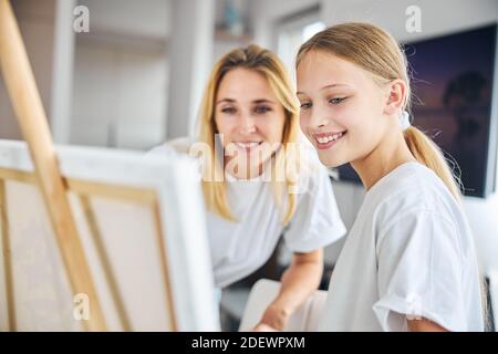 Sorridente pittore ragazza e sua madre appoggiata verso il cavalletto Foto Stock